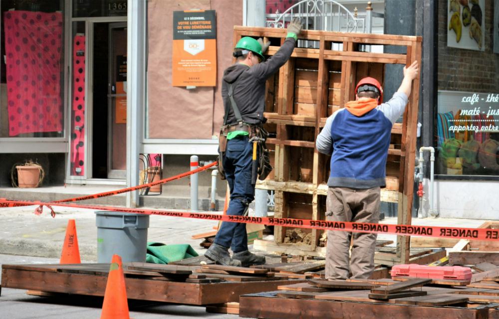 Two construction workers raising a wooden frame on a Montreal street