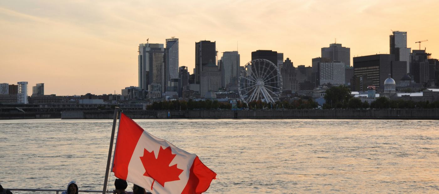 The Montreal skyline at sunset, seen from the St. Lawrence, with a Canadian flag flying from a boat